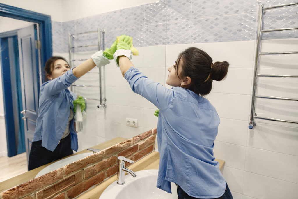 Mulher limpando o vidro de um banheiro simbolizando uso de produtos de limpeza